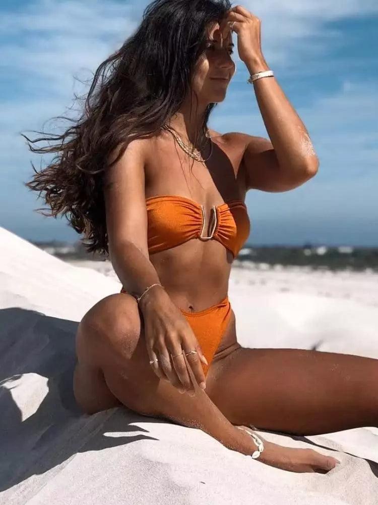 Esta imagem mostra uma mulher em um biquini laranja brilhante sentada em uma praia com o oceano visível ao fundo