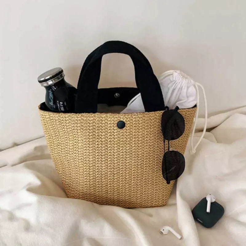 Bolsa de palha com alças pretas organizada com garrafa, óculos e acessórios do dia a dia
