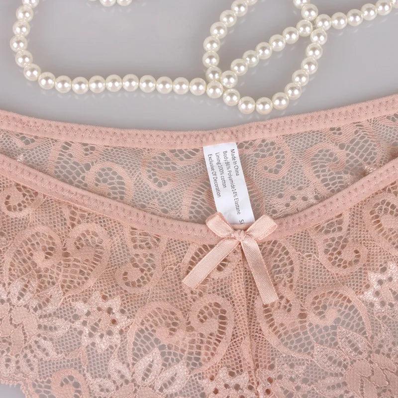 Detalhe de calcinha rosa claro em renda delicada com laço e etiqueta, decorada com colar de pérolas.