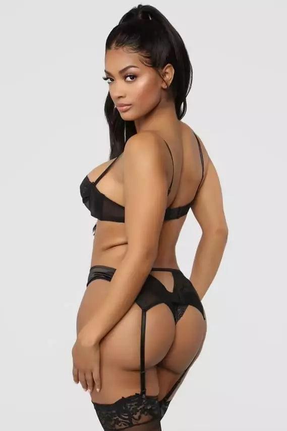 Vista traseira de conjunto lingerie preto com calcinha fio dental, cinta liga e detalhes em renda.