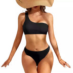Mulher em biquíni preto canelado com top de um ombro só e chapéu de palha, pose elegante para praia