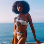 Mulher de cabelo afro com biquíni feminino branco e preto na praia ao entardecer