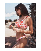 Mulher de praia na praia com conjunto de biquini com estampa de leopardo em vermelho e branco