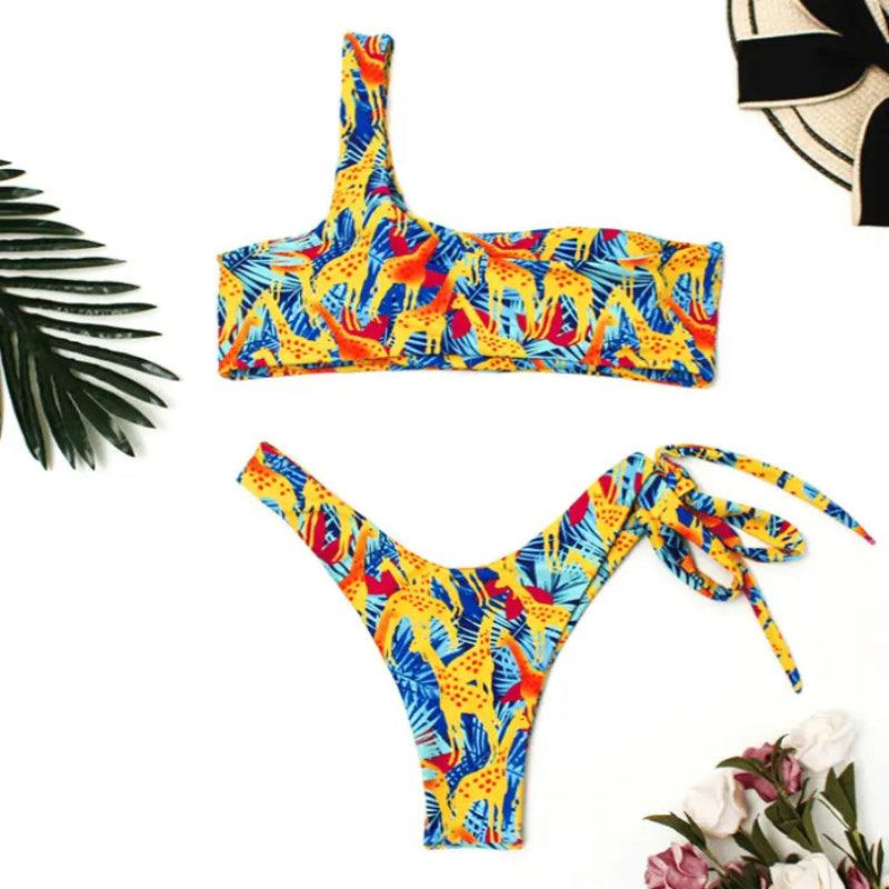 Biquíni estampado tropical em amarelo, azul e vermelho, modelo um ombro só e calcinha cavada com amarração lateral.