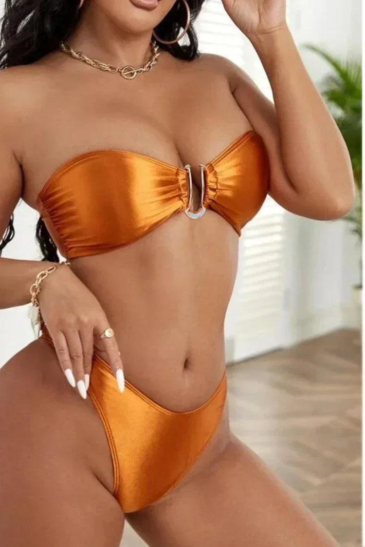 Biquíni bronze metálico com top tomara-que-caia e detalhe de argola central, acompanhado de colar dourado