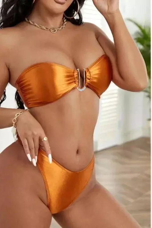 Biquíni bronze metálico com top tomara-que-caia e detalhe de argola central, acompanhado de colar dourado