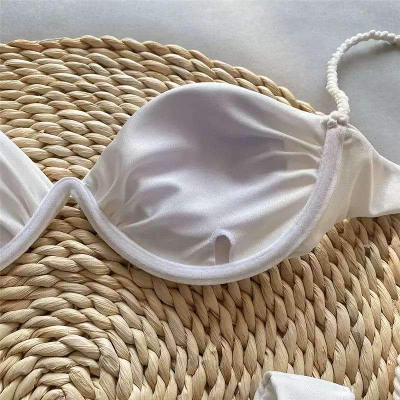 Bojo de biquíni branco com alças e detalhes trançados sobre base de palha natural