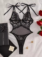 Lingerie preta de renda com sutiã strappy e calcinha fio dental, laços decorativos nos ombros.
