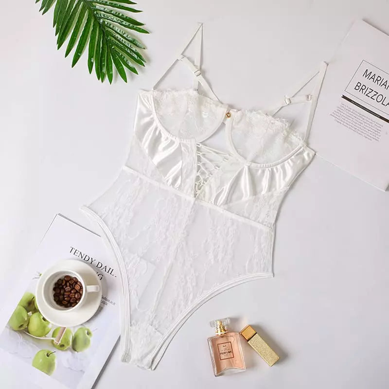 Body branco transparente com renda e bojo em flatlay com café, perfume, revista e folha de palmeira