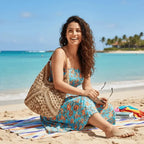 Mulher usando vestido floral azul turquesa com bolsa de crochê bege sentada na praia