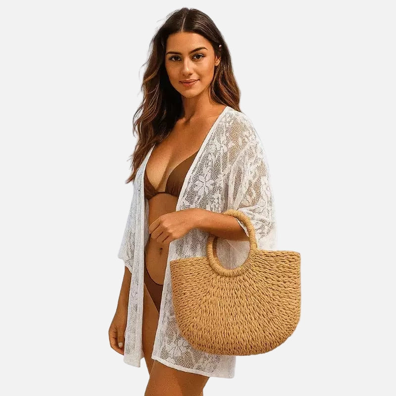 Mulher usando biquíni marrom com saída de praia branca rendada e bolsa de palha dourada