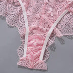 Close-up de calcinha rosa em renda delicada com acabamento em elástico branco e detalhes florais em relevo.