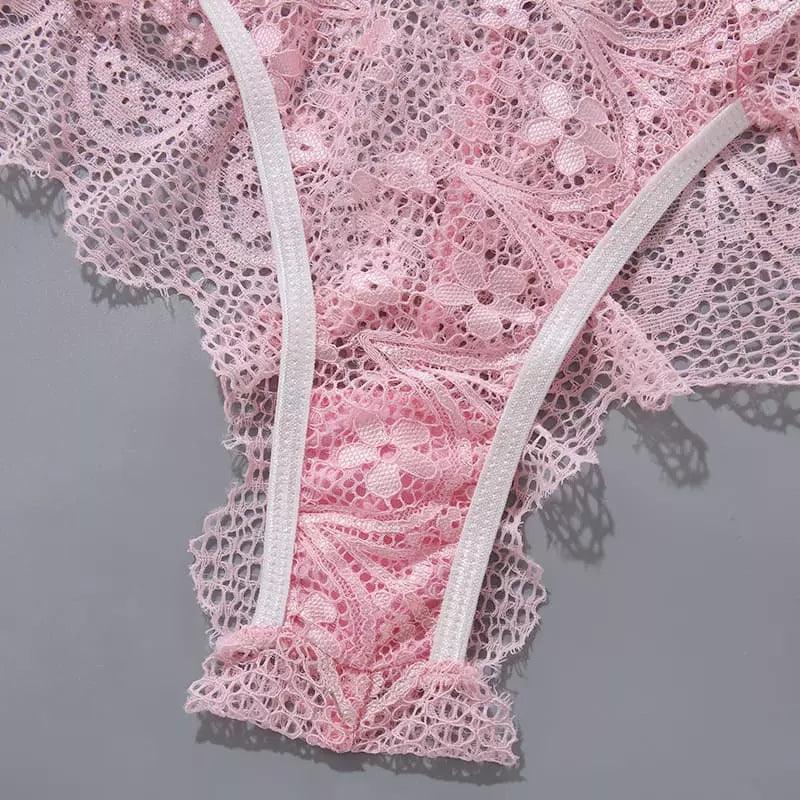 Close-up de calcinha rosa em renda delicada com acabamento em elástico branco e detalhes florais em relevo.