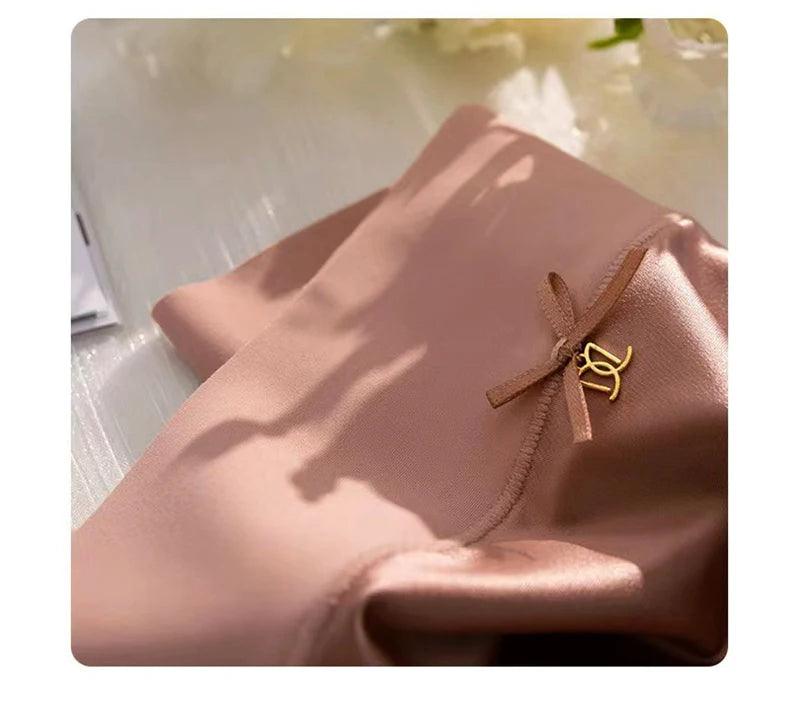 Calcinha rosa nude de cetim com laço delicado e pingente dourado, detalhe de acabamento costurado lateral