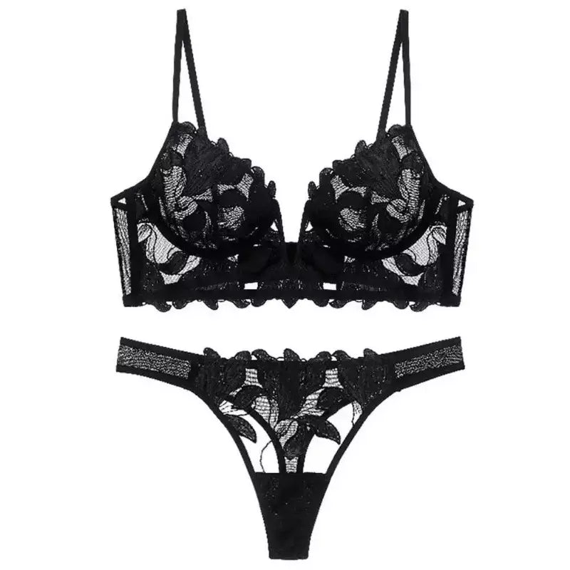 Conjunto de lingerie preto com renda floral transparente, sutiã meia taça e calcinha fio dental com acabamento ondulado.