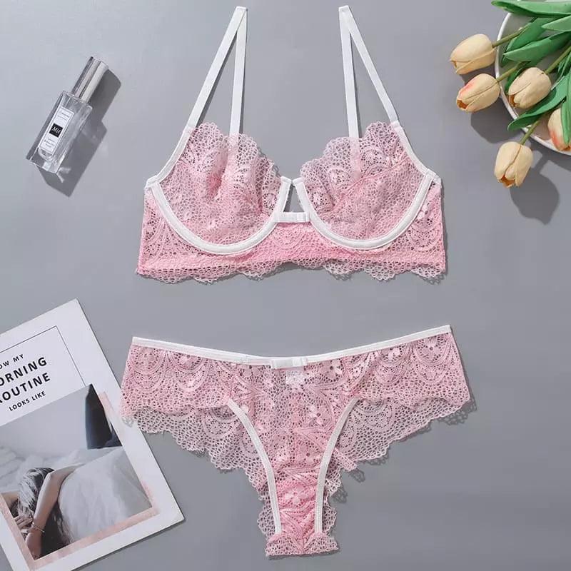 Conjunto lingerie rosa em renda com detalhes brancos, fotografado em fundo cinza com tulipas e perfume como decoração