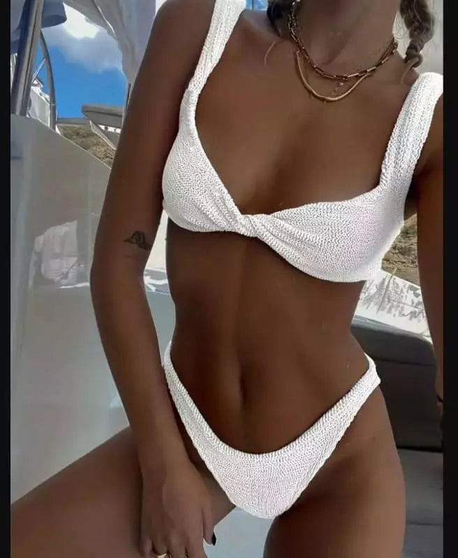 Biquíni branco texturizado modelo asa delta, com alças largas e detalhes em relevo, colar dourado em camadas.