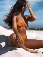 Esta imagem mostra uma mulher em um biquini laranja brilhante sentada em uma praia com o oceano visível ao fundo