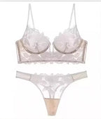 Conjunto de lingerie branca com renda floral transparente, sutiã meia taça e calcinha fio dental com acabamento ondulado.