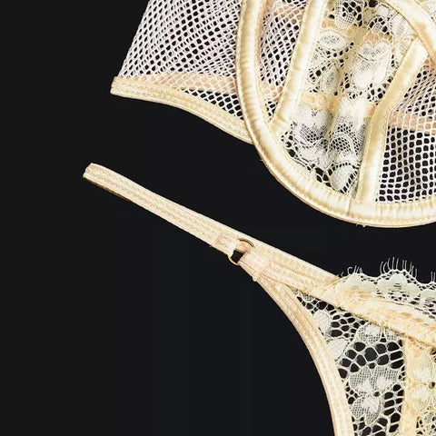 Detalhe de lingerie nude com renda delicada em tela vazada e acabamento acetinado dourado.