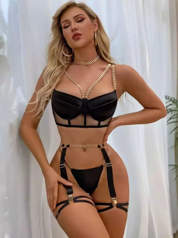 Lingerie preta sensual com sutiã transparente, correntes douradas e cinta liga com detalhes metálicos