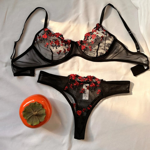 O conjunto de lingerie é composto por um sutiã e uma calcinha com uma estampa floral vermelha elaborada em um tecido semi-transparente preto