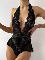 Body preto rendado com decote profundo, laço cetim na cintura e babado transparente.