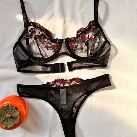 O conjunto de lingerie é composto por um sutiã e uma calcinha com uma elaborada estampa floral vermelha em um tecido semi-transparente preto