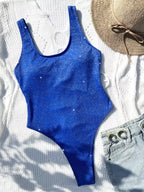 Maiô azul brilhante inteiro com alças largas, combinado com chapéu de palha e shorts jeans