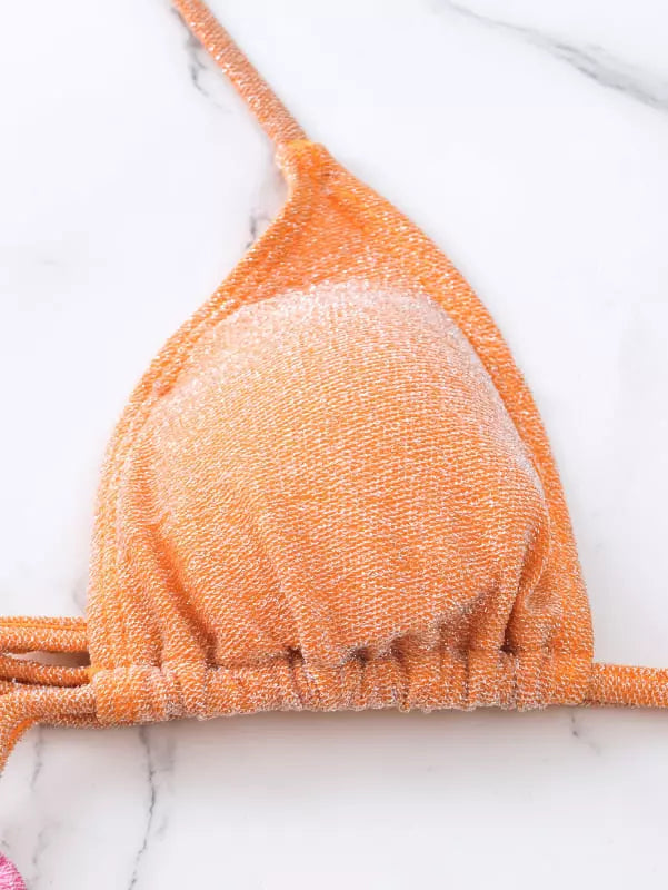 Detalhe close-up top biquíni laranja com brilho e textura sobre mármore branco