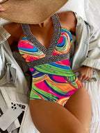 Maiô colorido com estampa abstrata em tons neon, alças em correntes prateadas, chapéu de palha e jaqueta clara.