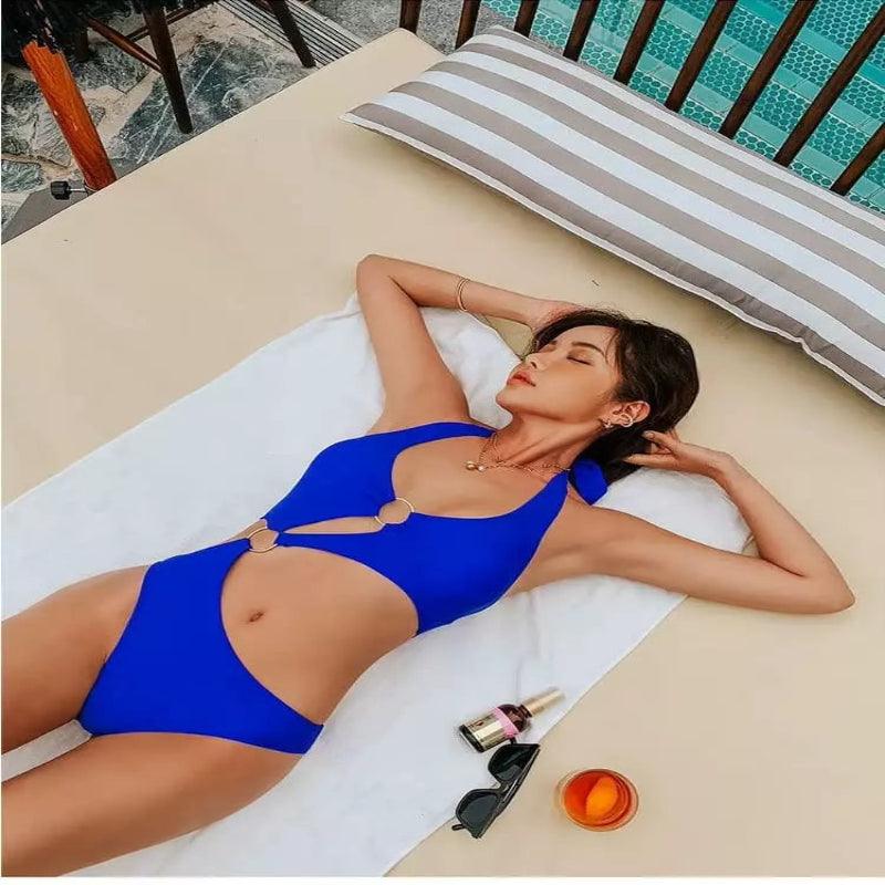 Maiô azul royal com detalhes em argolas douradas, recortes modernos na barriga, estilo monoquíni para praia e piscina.