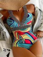 Maiô moderno com estampa colorida, alças em correntes prateadas, chapéu de palha e jaqueta cinza claro.