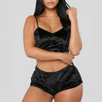 A imagem mostra um conjunto de pijama curto em veludo preto, com top de alças e shorts, em fundo neutro cinza claro.