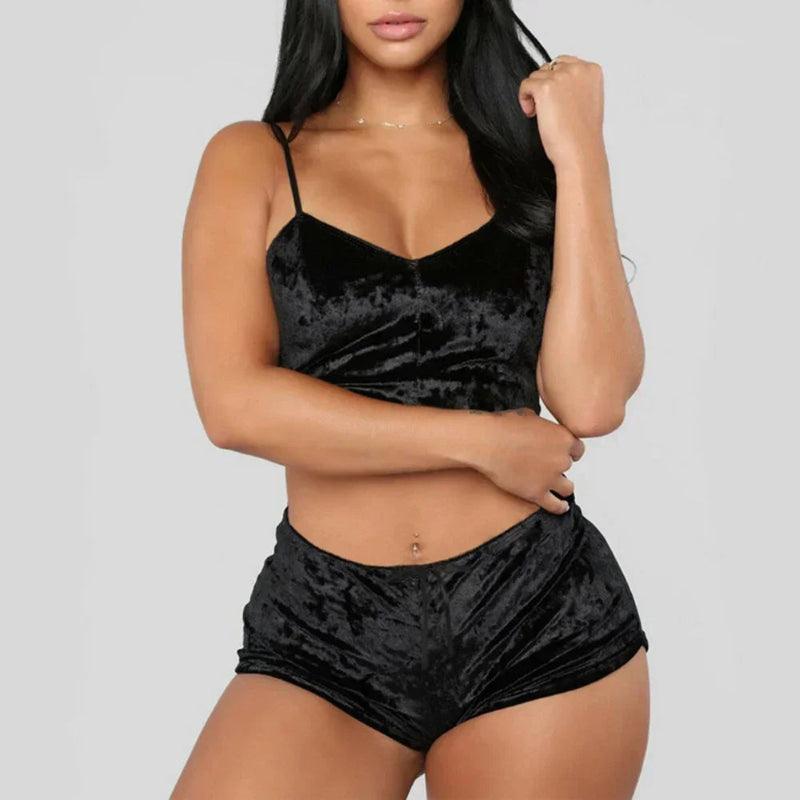 A imagem mostra um conjunto de pijama curto em veludo preto, com top de alças e shorts, em fundo neutro cinza claro.