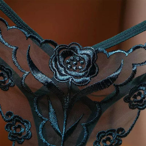 Detalhe de calcinha em renda verde escura, com bordado floral metálico sobre tule transparente.